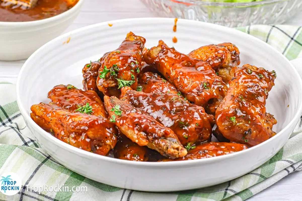 Pub-style BBQ chicken wings served in a white bowl next to a bowl of tangy sauce.