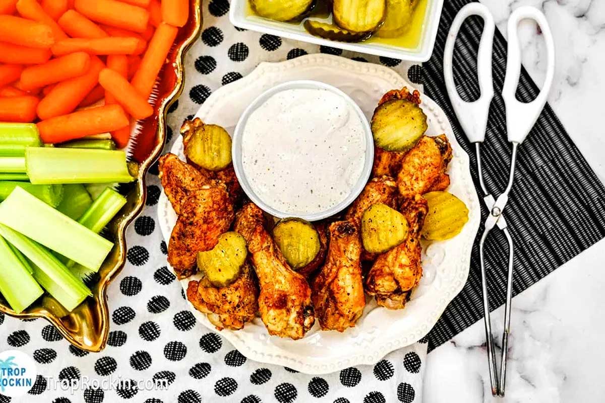 A plate of pub food with chicken wings, carrots, celery and dip.