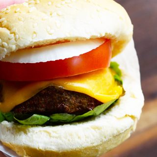 A person holding a burger topped with cheese and tomatoes, cooked using an air fryer.