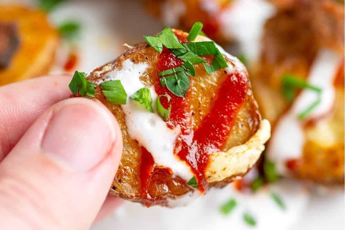 A person holding up a plate of potato chips with ketchup and sour cream.