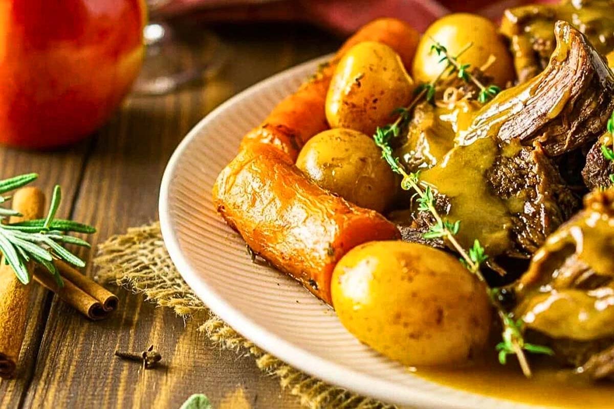 A plate with roast beef, potatoes, and carrots drizzled in apple cider gravy.