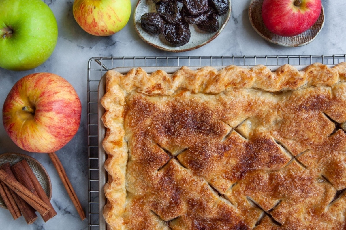 Apple pie on a cooling rack with apples and cinnamon, perfect for Thanksgiving.