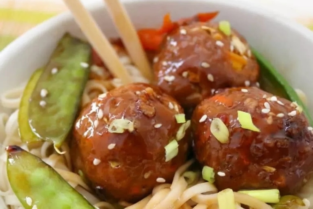 Asian meatballs in a white bowl with chopsticks.