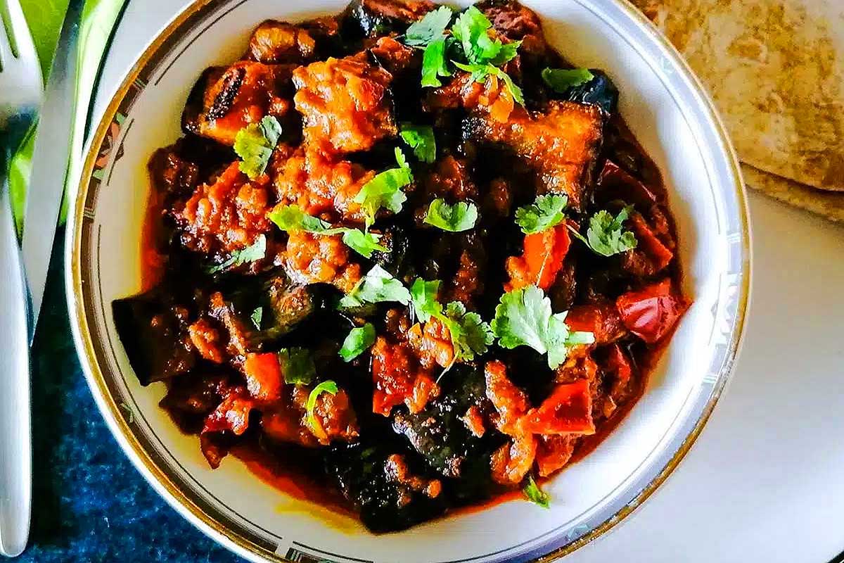A bowl of eggplant curry on a table with a fork.