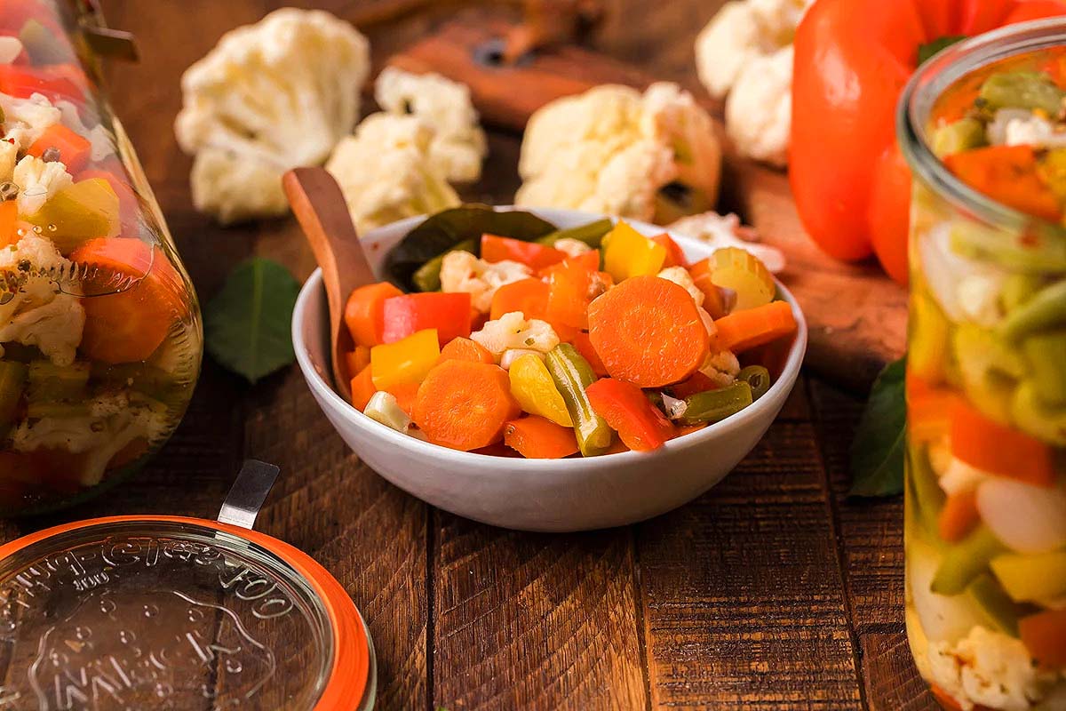 Italian pickled vegetables in jars on a wooden table.