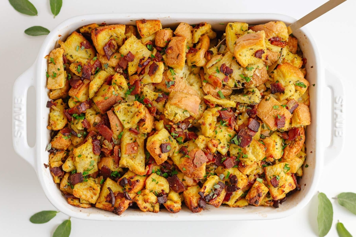 Bacon and sausage stuffing recipes in a white dish with sprigs of sage.