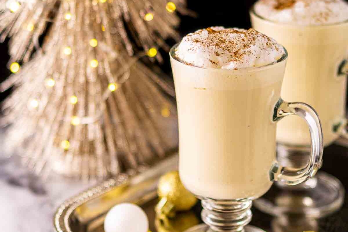 Two mugs of hot cocoa with whipped cream and cinnamon on a tray, perfect for cozy winter recipes.