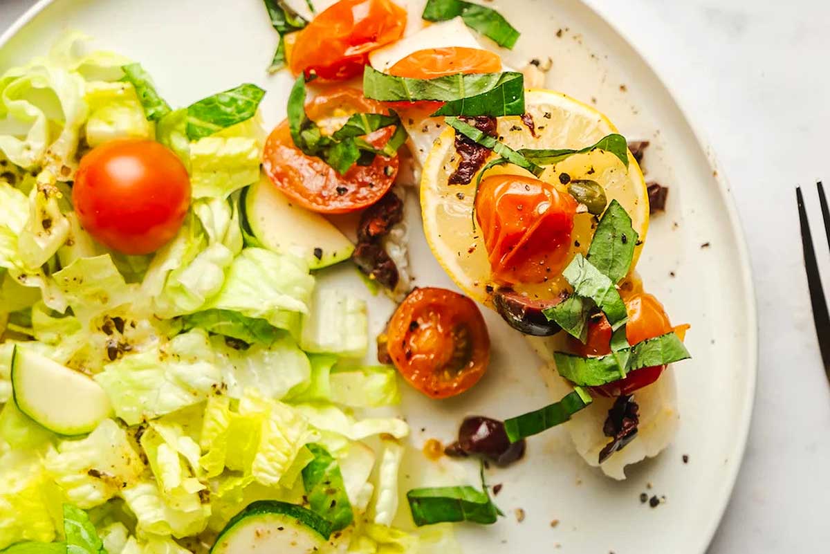 A plate with fish, tomatoes, lettuce and olives.