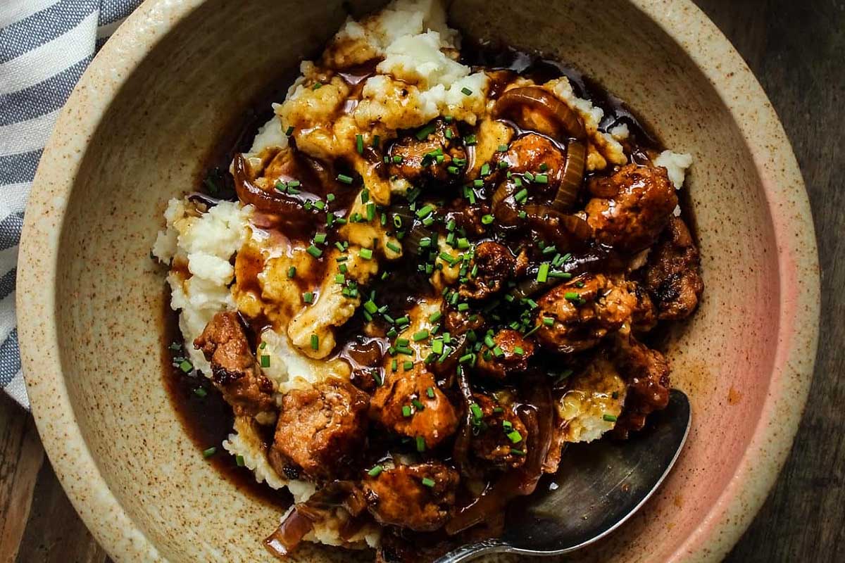 A bowl of mashed potatoes with meat and gravy.