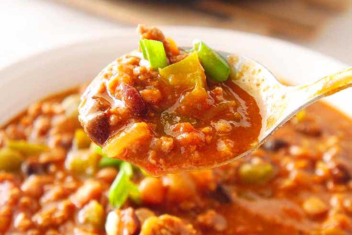 A spoon is being held up to a bowl of chili.