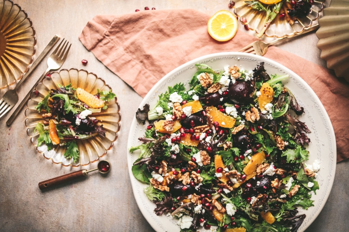 A bowl of salad with oranges, walnuts and pomegranate as sides.