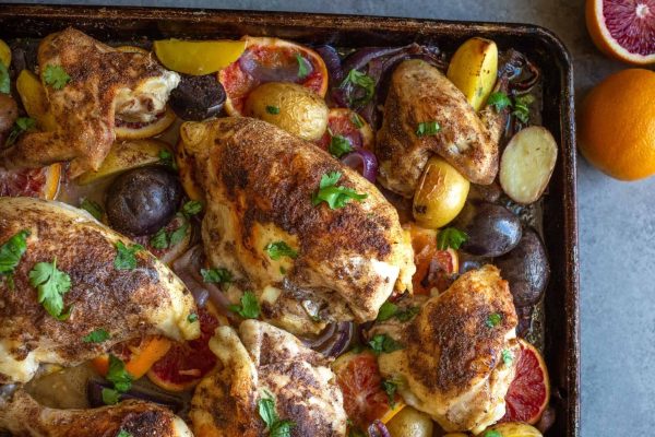 Bone-in roasted chicken breasts with blood oranges and potatoes on a baking sheet.