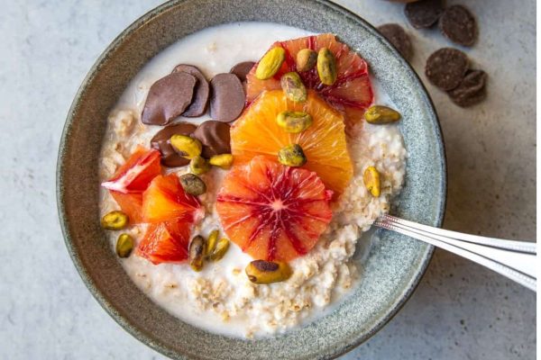A bowl of oatmeal with fruit (oranges) and pistachios.
