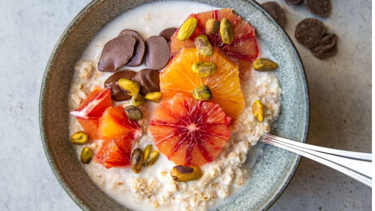 A bowl of oatmeal with fruit (oranges) and pistachios.