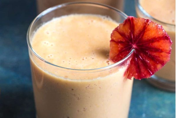 A glass of orange smoothie with a slice of orange, perfect for those seeking refreshing and citrusy recipes.