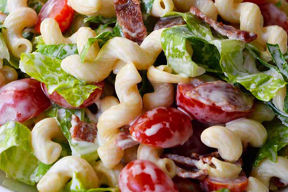 A bowl of pasta salad with bacon, tomatoes and lettuce.