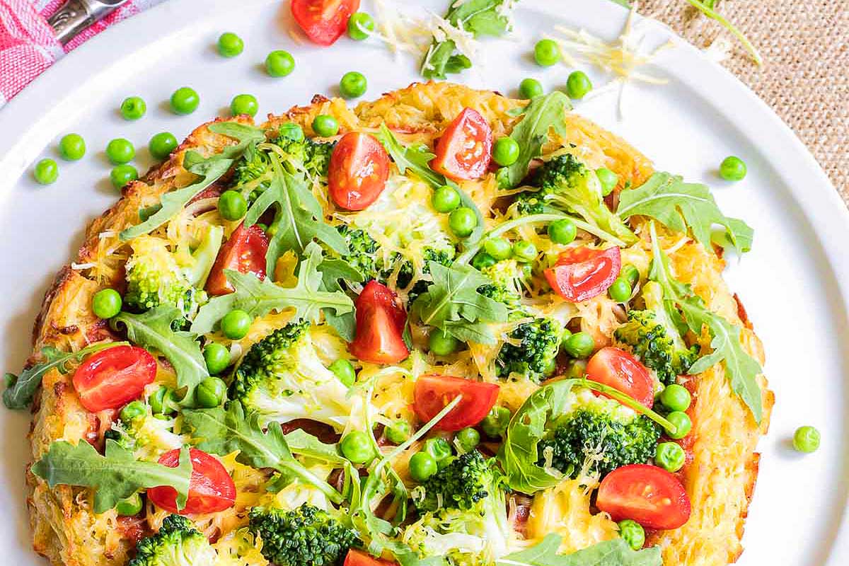 A brunch pizza with broccoli, tomatoes, and peas on a plate.