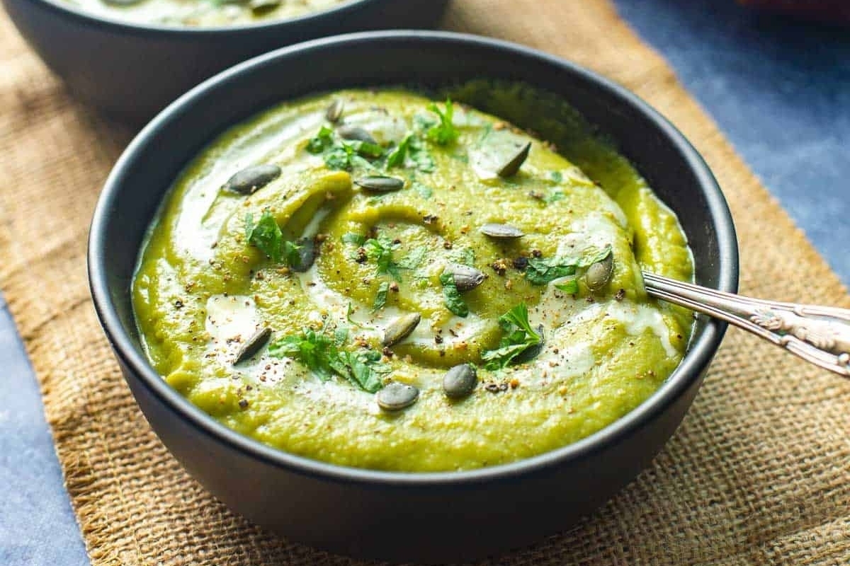 Two bowls of vibrant green soup with a spoon, made from recipes using frozen peas.