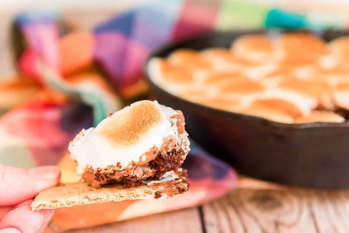 A person holding a graham cracker in front of a pan of s'mores dip.