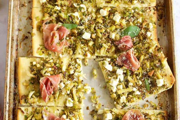 A baking sheet with a pizza with arugula and prosciutto.