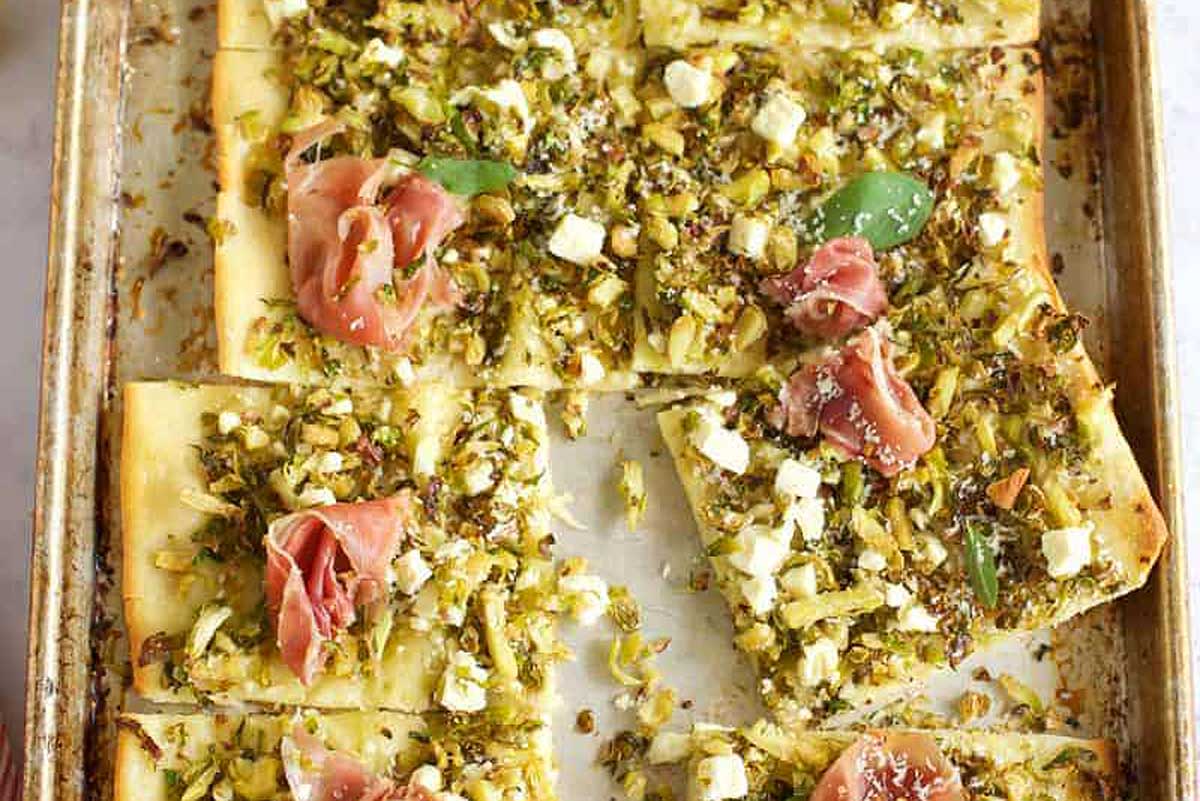 A baking sheet with a pizza with arugula and prosciutto.