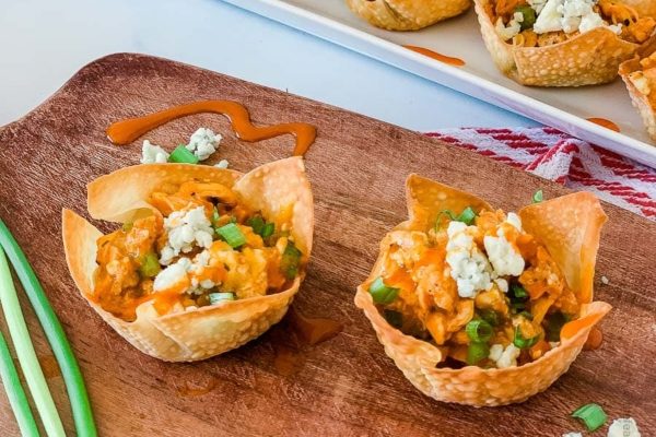 Buffalo chicken cups with blue cheese and green onions on a wooden cutting board.