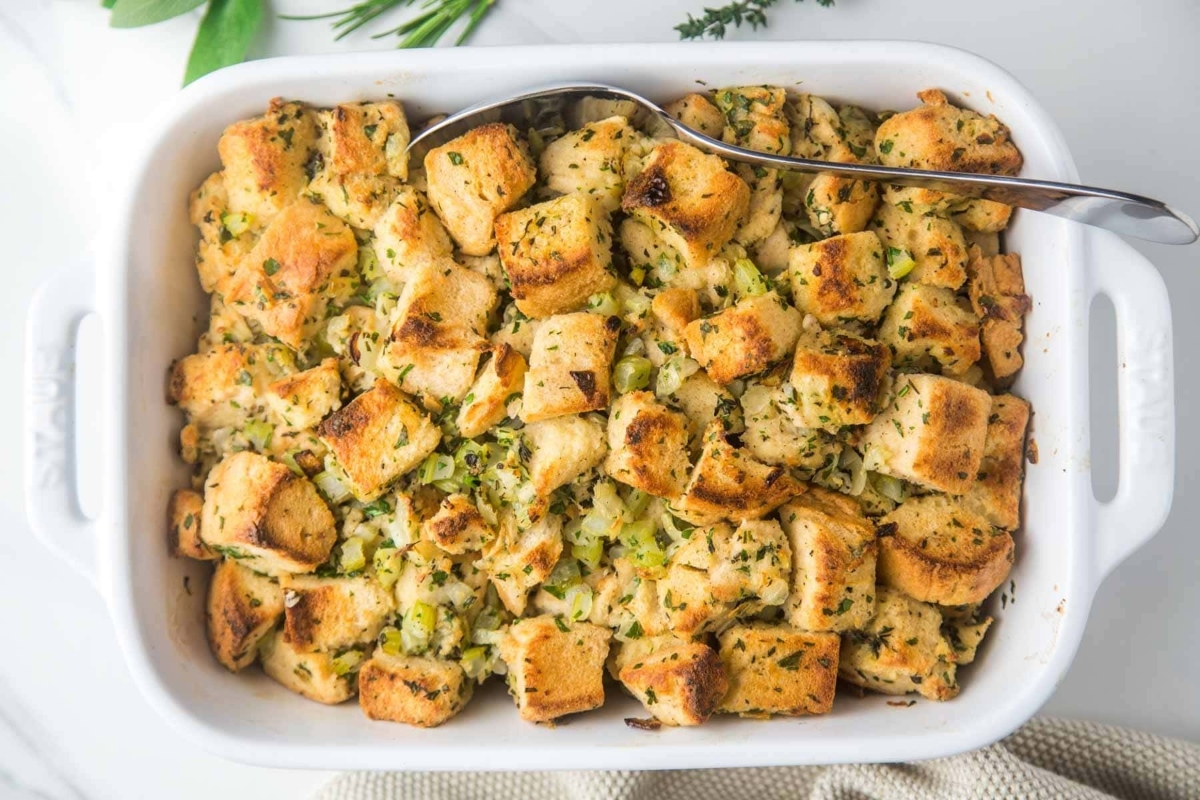 Bread stuffing recipe in a white baking dish with a spoon.