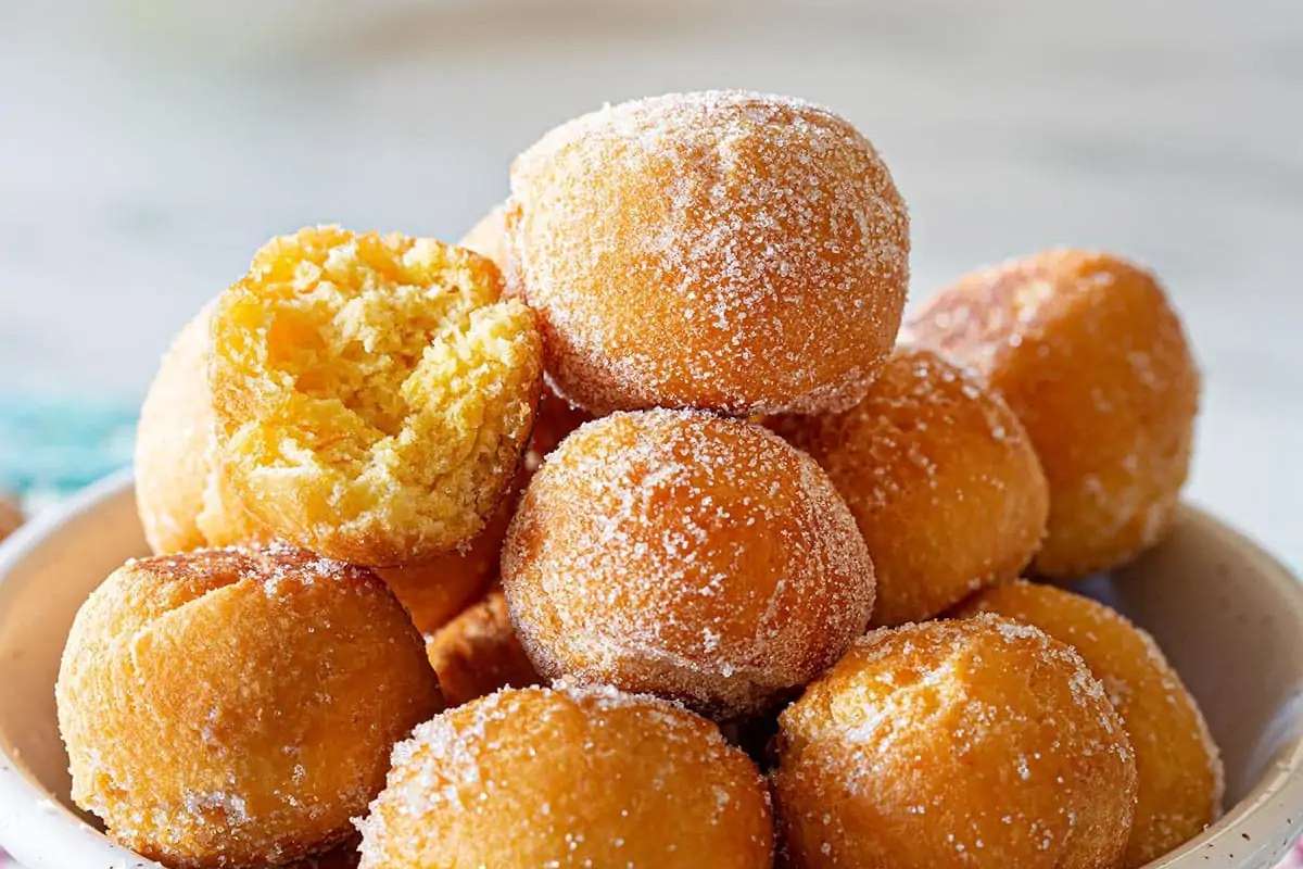 An Italian dessert concept featuring a bowl of sugared doughnuts with a bite taken out.