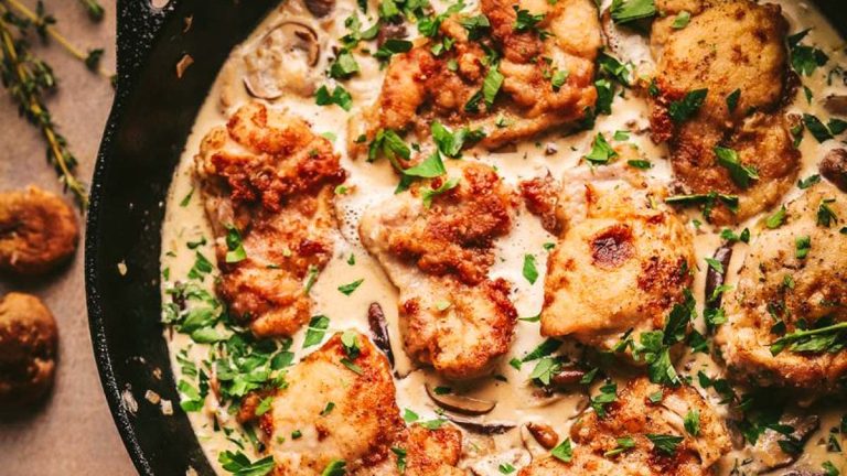 Champagne chicken in mushroom sauce cooked in a skillet on a wooden table.