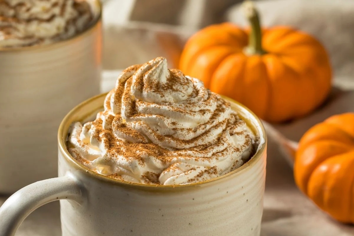 Two Starbucks pumpkin spice lattes with whipped cream and pumpkins, perfect for the holiday season.