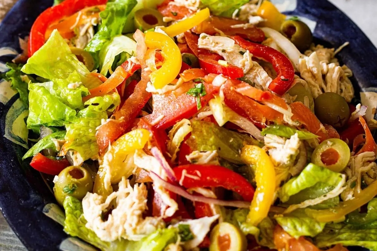 A salad with chicken, peppers and olives on a plate.
