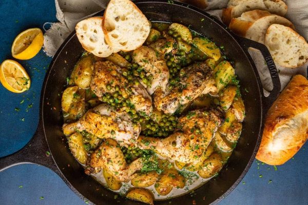 Bone-in chicken with potatoes and peas in a skillet on a blue background.
