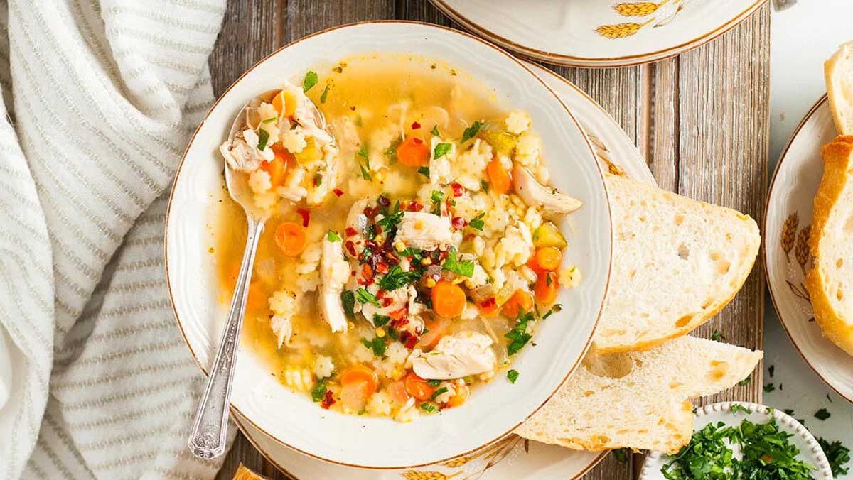 A bowl of chicken soup and bread on a table.