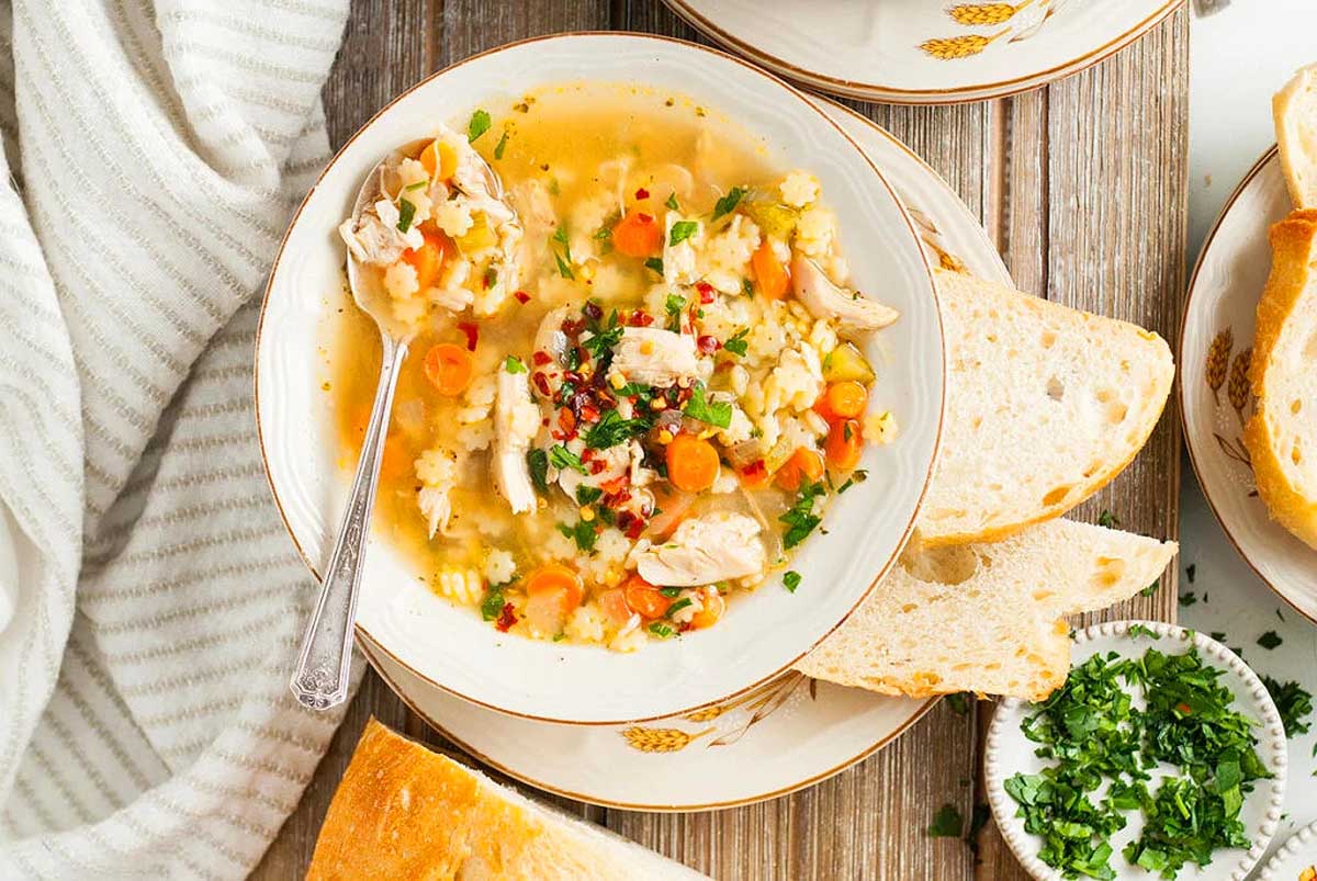 A bowl of chicken soup and bread on a table.