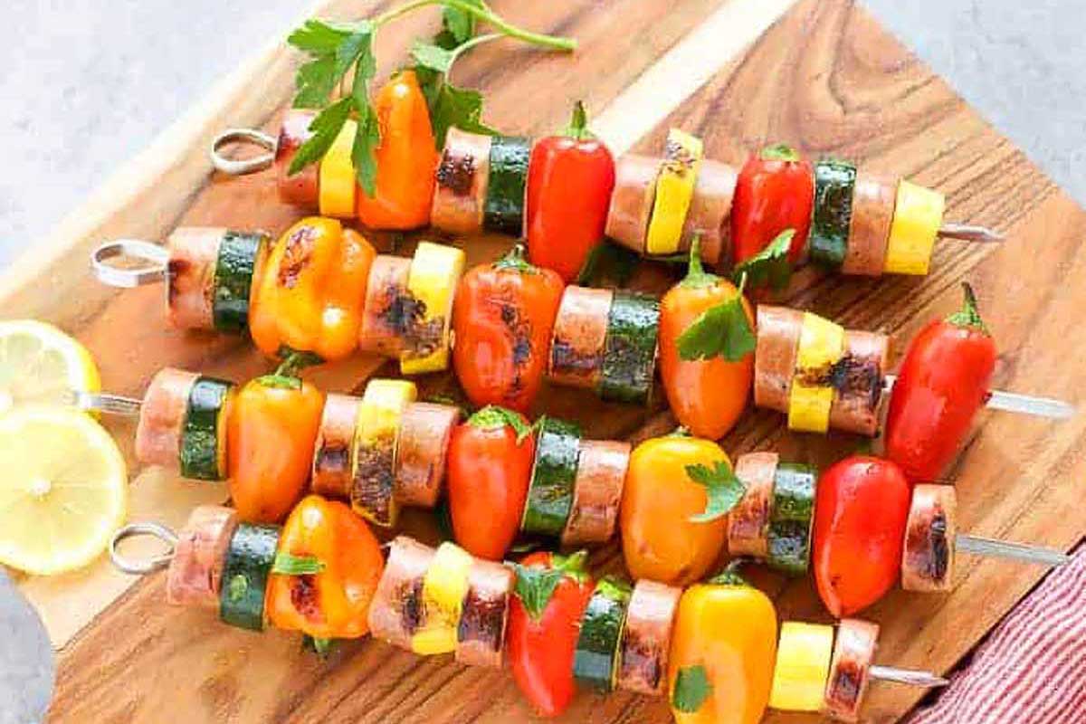 Skewers of vegetables and sausage on a wooden cutting board.