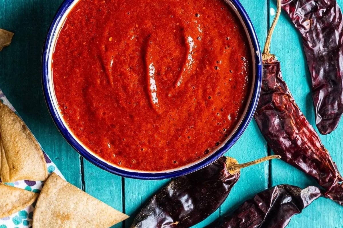 A bowl of mexican sauce with chips and tortillas.