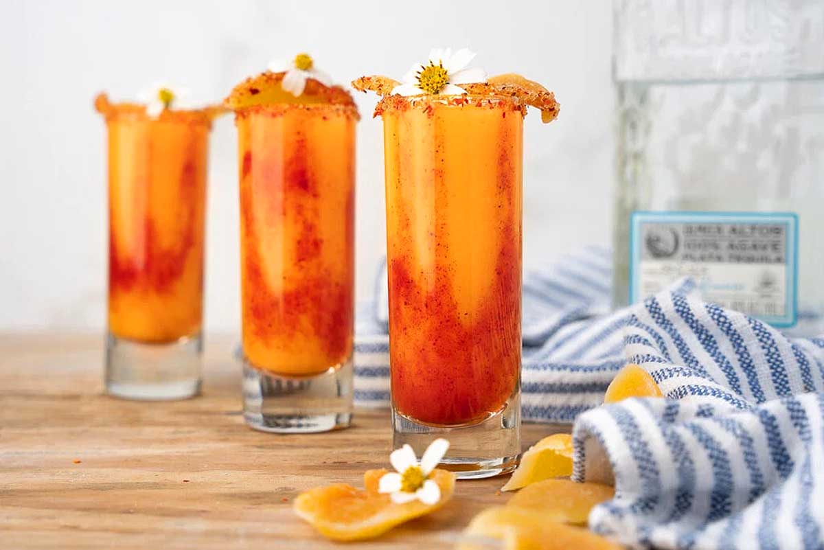 Three glasses with orange juice and a bottle of tequila.
