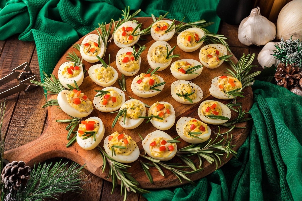Appetizing deviled eggs on a wooden board with sprigs of rosemary.