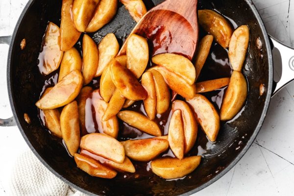 Apple slices in a frying pan with a wooden spoon.