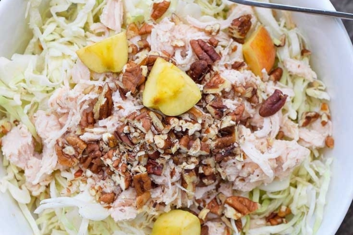 Coleslaw salad with chicken and pecans in a white bowl.