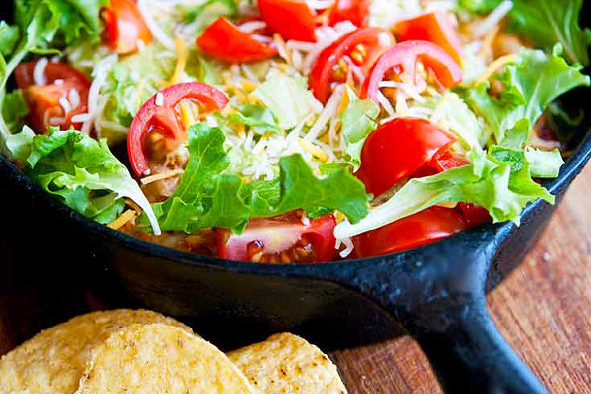 A skillet filled with a salad and chips.