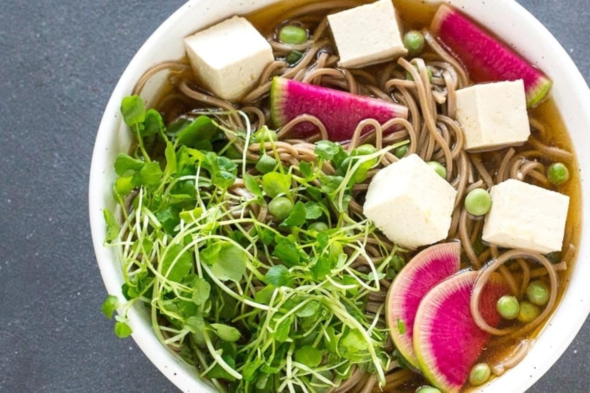 A flavorful bowl of noodle soup with radishes, tofu, and frozen peas.