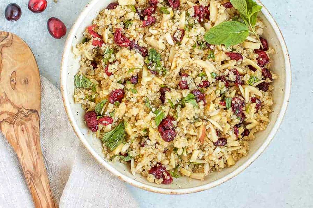 Cranberry quinoa salad in a bowl with a wooden spoon.