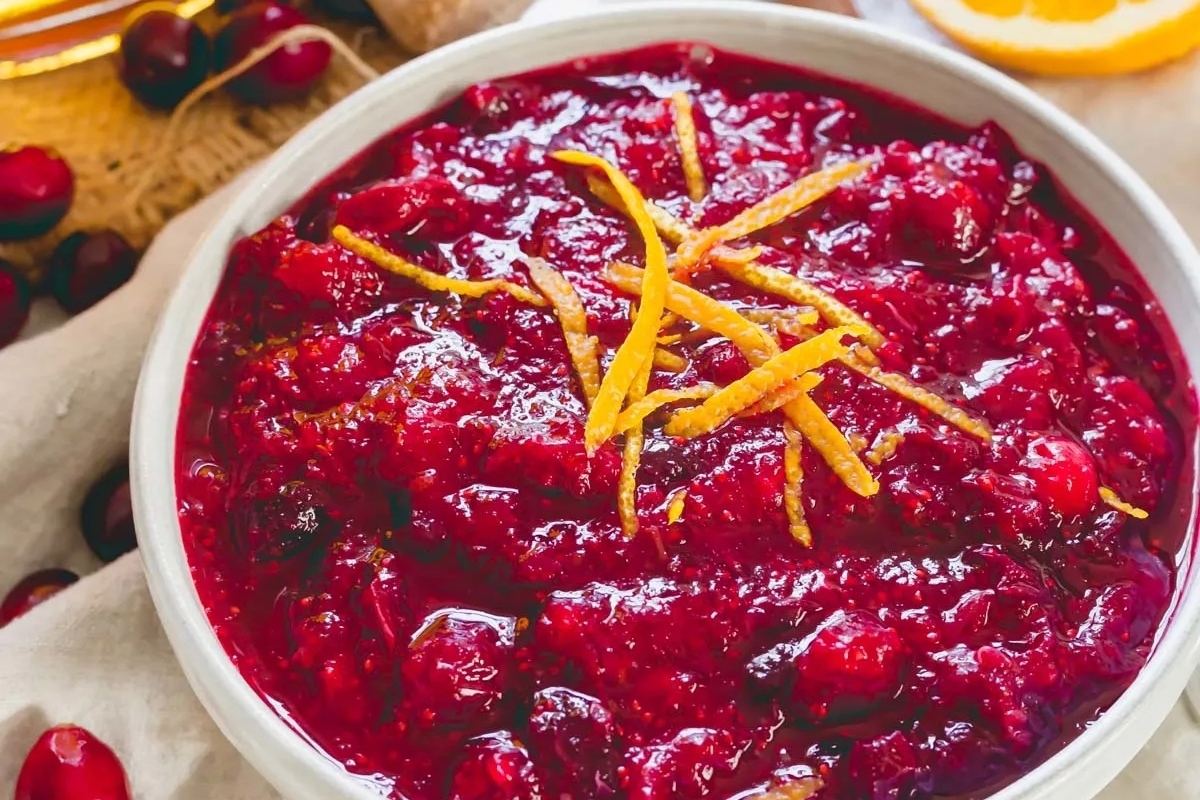 Delicious cranberry sauce recipe served in a white bowl, accompanied by vibrant orange slices.