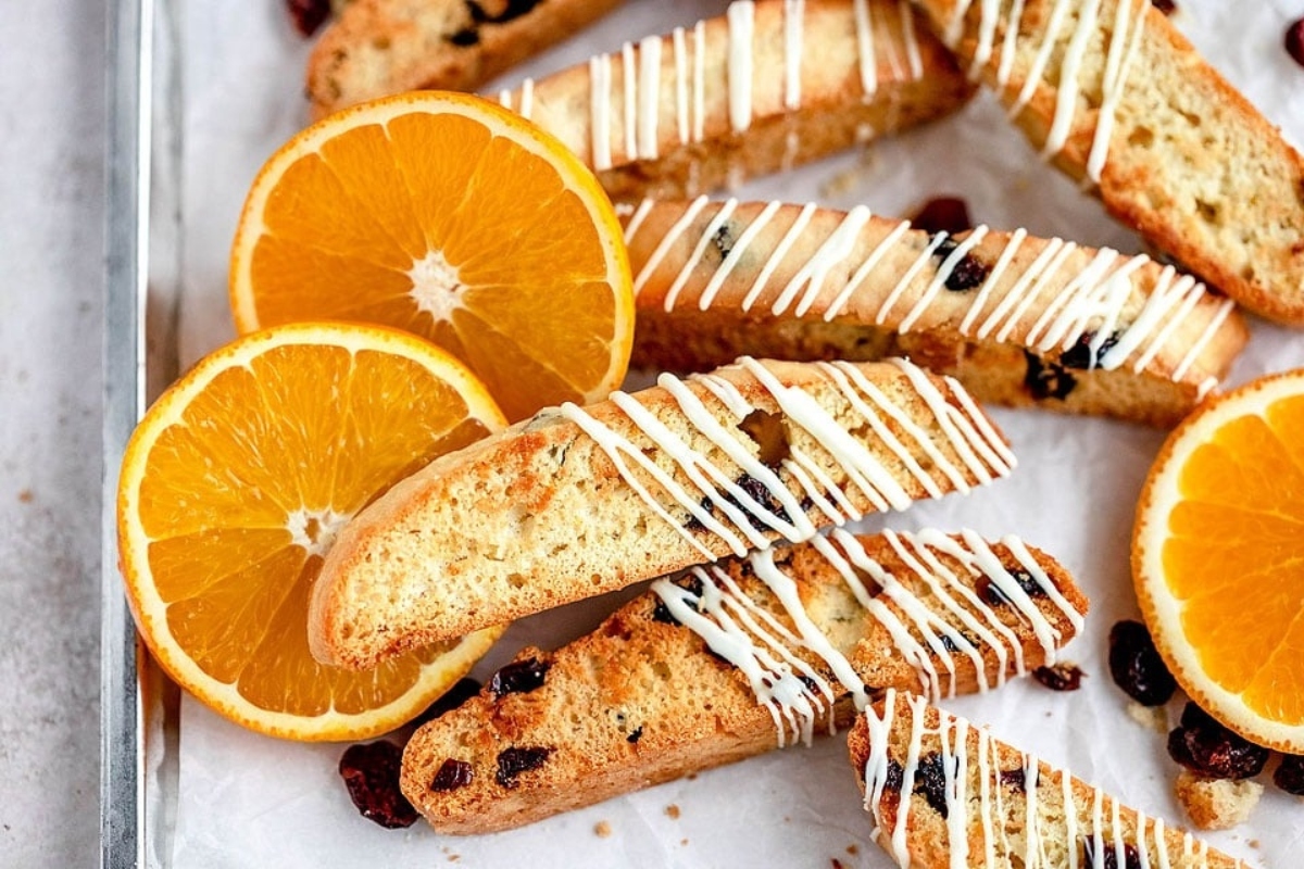 Orange and raisin biscotti with a drizzle of white chocolate on a baking sheet.