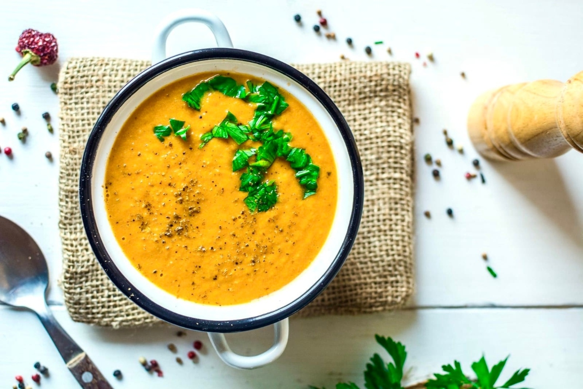 A cheap potluck dish - a bowl of carrot soup with parsley and a spoon.