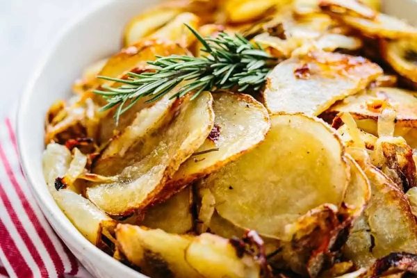 Thanksgiving roasted potatoes in a white bowl with rosemary sprig.