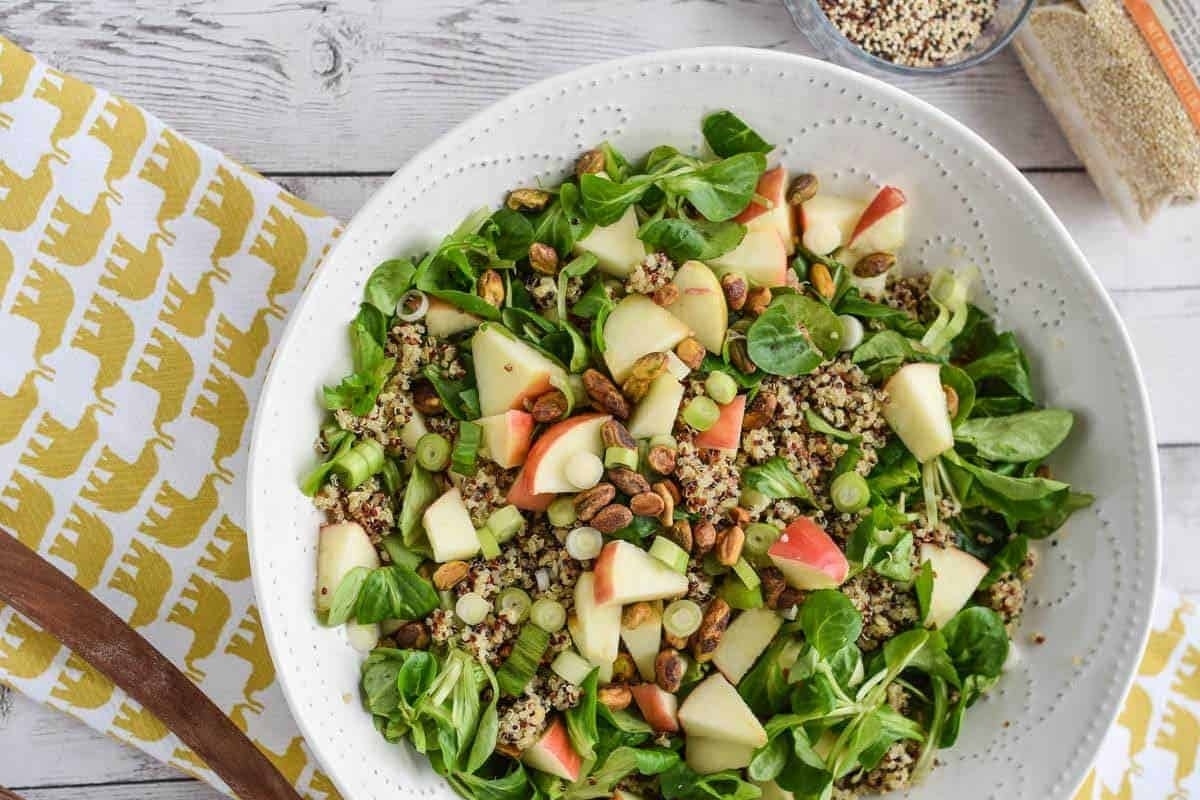 A bowl of salad with apples, quinoa and nuts.