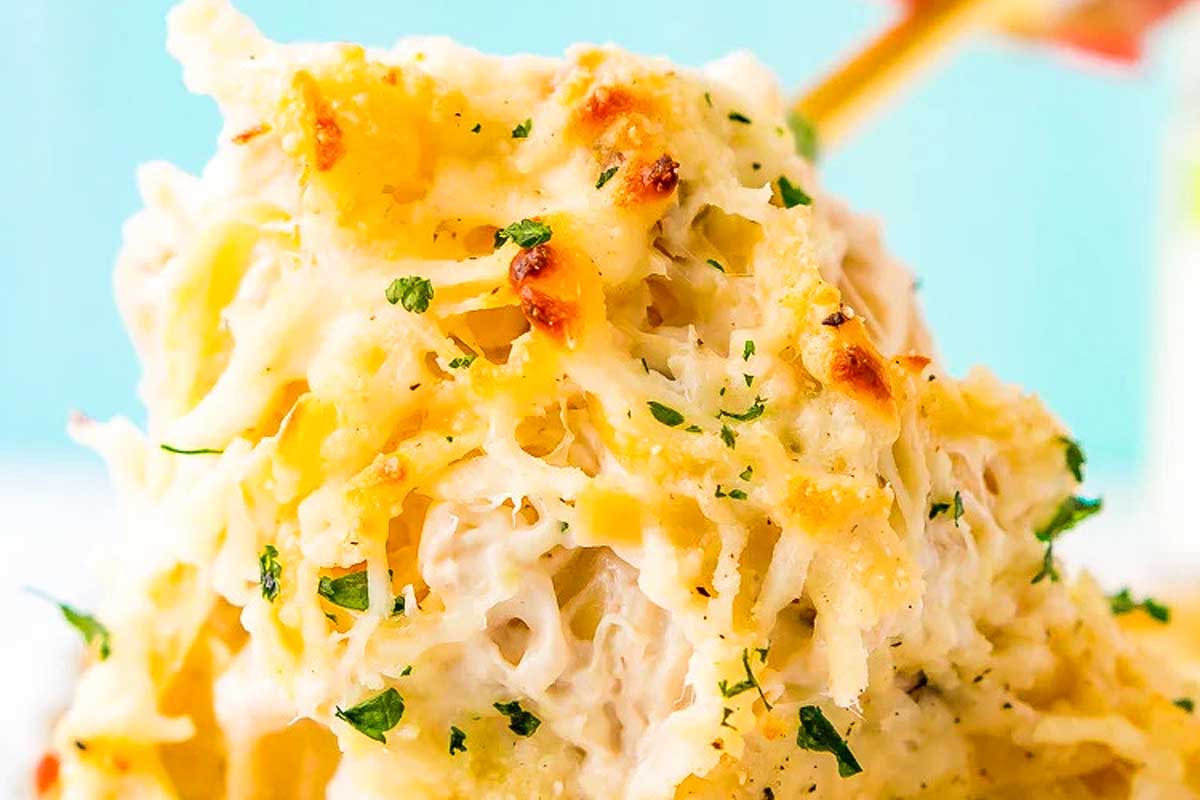 A person is holding a piece of cheesy chicken pasta.
