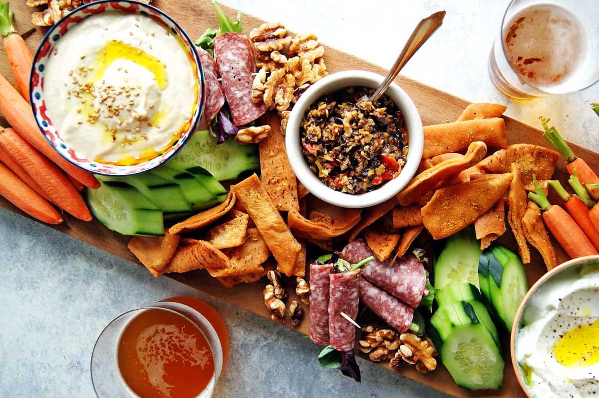 A tray of dips and snacks on a wooden board.